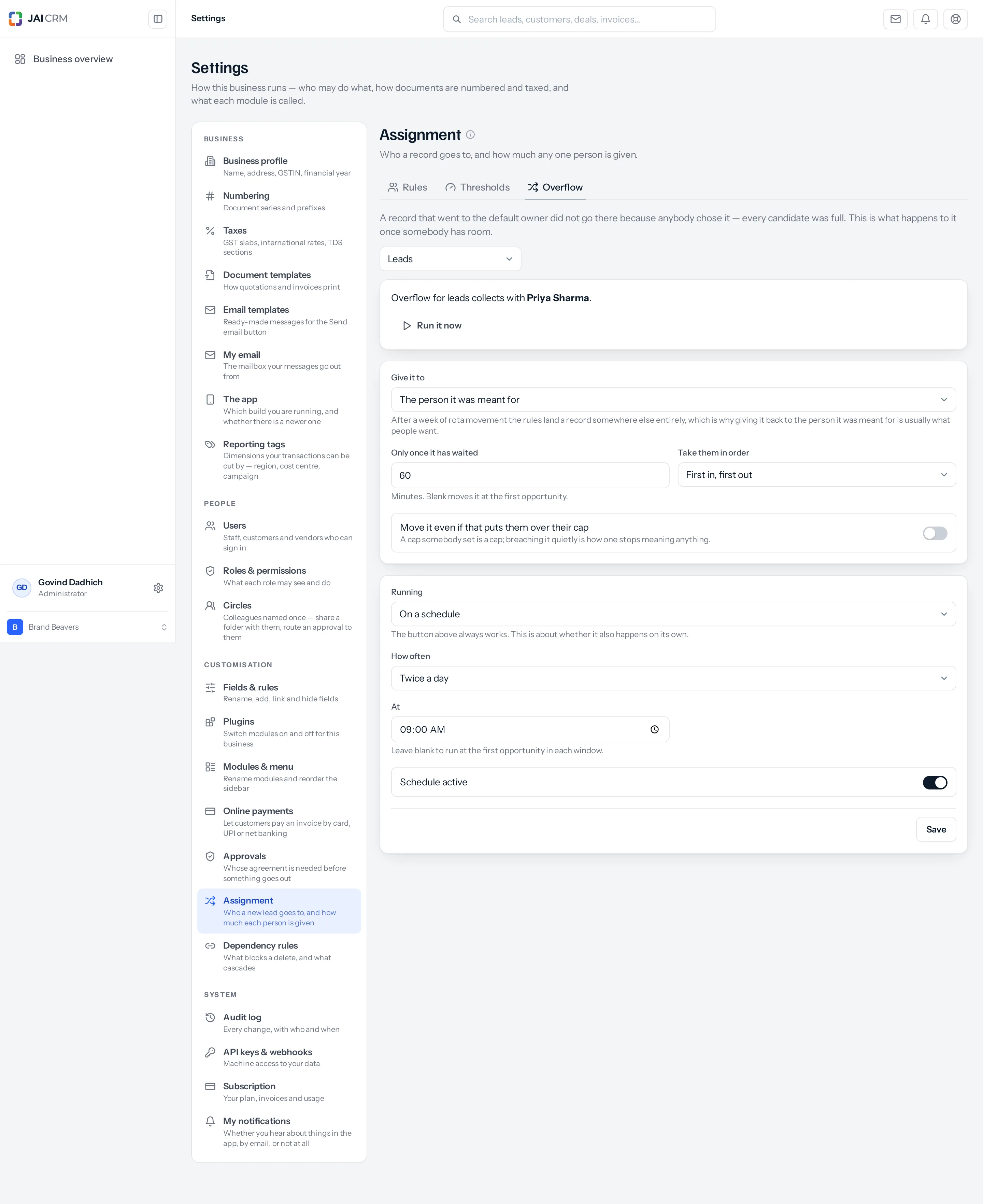 The Assignment Overflow tab. Under the blurb "A record that went to the default owner did not go there because anybody chose it — every candidate was full. This is what happens to it once somebody has room", a module picker reads Leads. A panel says "Overflow for leads collects with Priya Sharma" above a Run it now button. Below, "Give it to" reads "The person it was meant for", "Only once it has waited" reads 60 minutes, "Take them in order" reads "First in, first out", and a switch "Move it even if that puts them over their cap" is off. A second panel has Running set to "On a schedule", How often "Twice a day", At "09:00 AM", a "Schedule active" switch turned on, and a Save button.